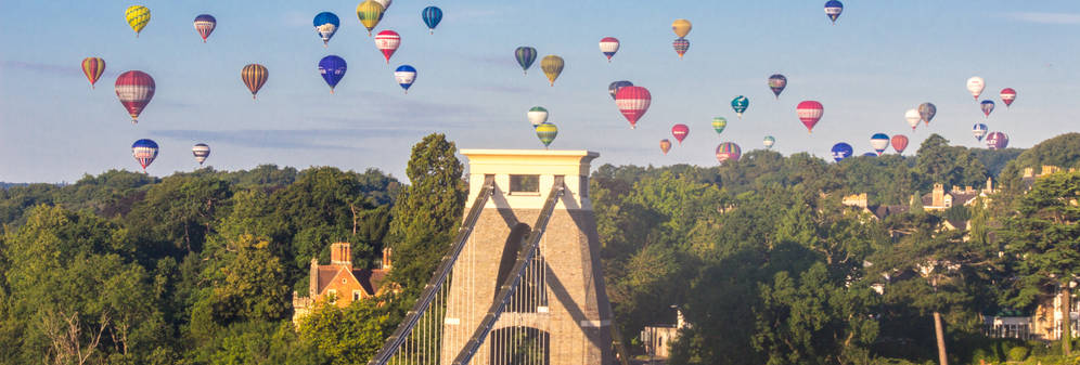 Clifton Suspension Bridge on a clear day with dozens of hot air balloons in the sky. 